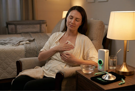 Breastfeeding mother applying warm compress to engorged breast for relief with silver nursing cups and bottle warmer visible on bedside table