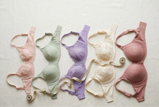 Five extended-size bras arranged on cream linen with fabric tape measure, featuring I cup sizing, inclusive sizing flat-lay