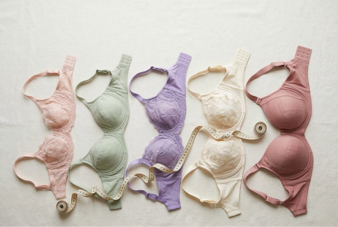 Five extended-size bras from D through O cup arranged in ascending order on cream linen with a fabric tape measure, inclusive sizing flat-lay