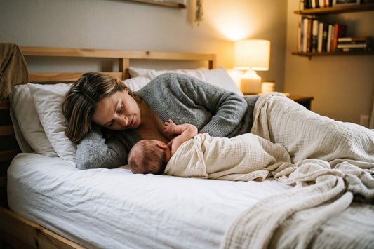 Mother and newborn lying on sides facing each other during side-lying breastfeeding in softly lit bedroom